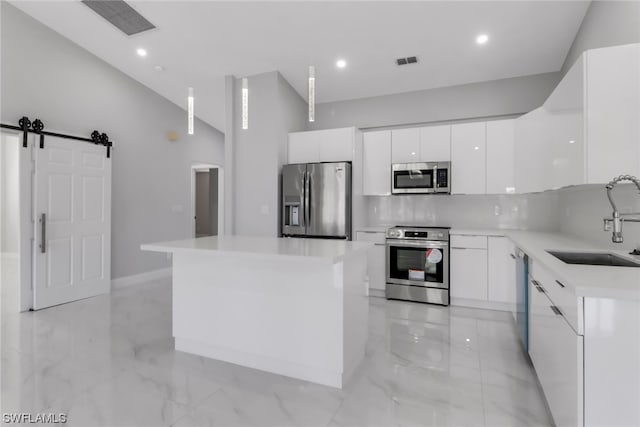 kitchen with tasteful backsplash, a barn door, white cabinets, stainless steel appliances, and sink