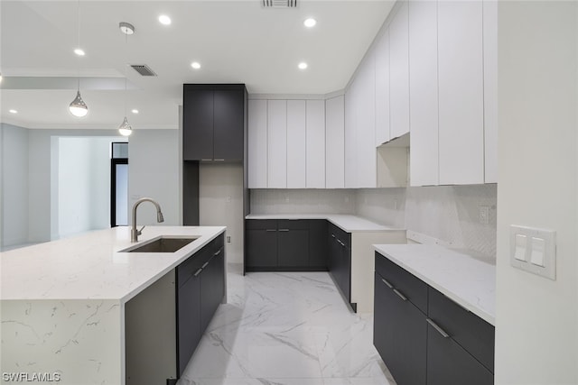 kitchen with light stone countertops, backsplash, a kitchen island with sink, sink, and pendant lighting