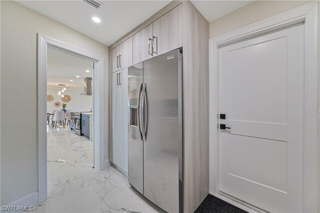 kitchen featuring wall chimney range hood and stainless steel refrigerator with ice dispenser