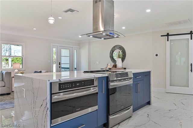 kitchen with blue cabinets, a barn door, appliances with stainless steel finishes, island range hood, and light stone counters