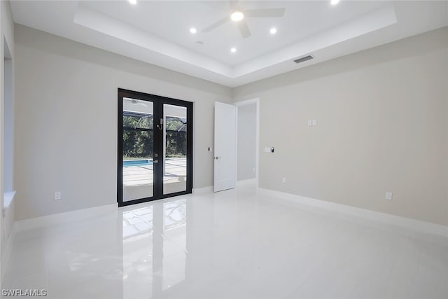 tiled empty room with french doors, ceiling fan, and a tray ceiling