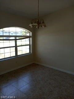 unfurnished room with dark tile flooring and a notable chandelier