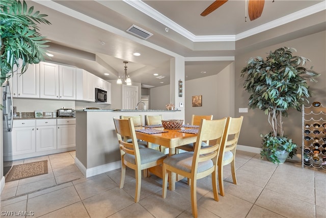 tiled dining room with a raised ceiling, ceiling fan, sink, and crown molding