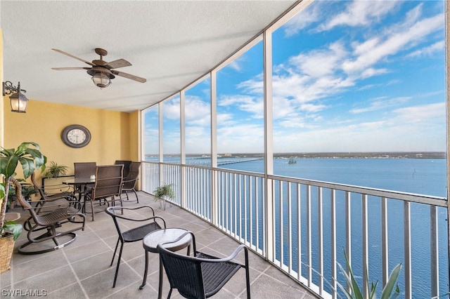 sunroom with ceiling fan and a water view