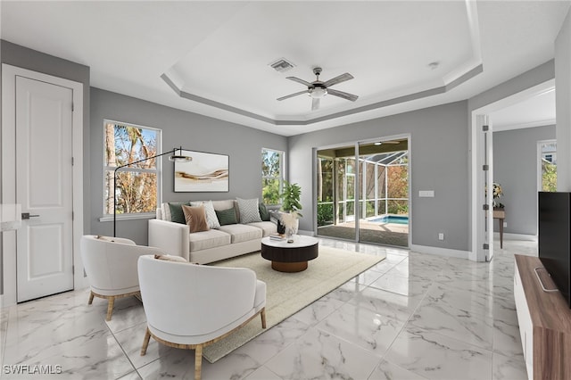 living room featuring a raised ceiling, ceiling fan, and a healthy amount of sunlight