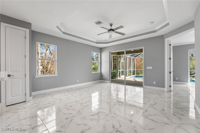 unfurnished room featuring a raised ceiling, ceiling fan, and a healthy amount of sunlight