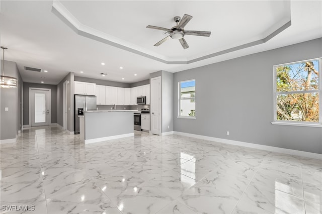 kitchen with hanging light fixtures, a raised ceiling, white cabinets, a kitchen island, and appliances with stainless steel finishes