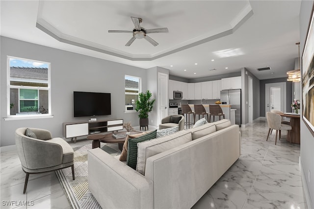 living room with a raised ceiling, ceiling fan, and ornamental molding