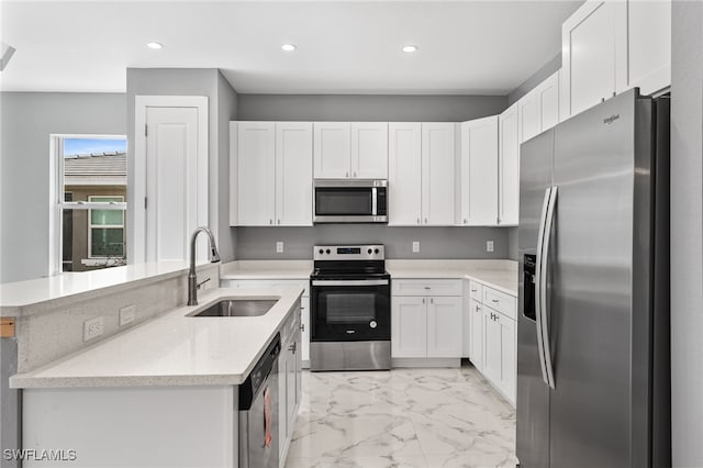 kitchen with kitchen peninsula, appliances with stainless steel finishes, light stone counters, sink, and white cabinetry