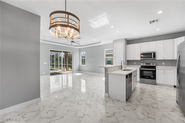 kitchen featuring pendant lighting, ceiling fan with notable chandelier, sink, appliances with stainless steel finishes, and white cabinetry