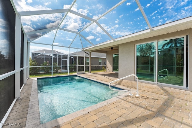 view of swimming pool featuring glass enclosure, ceiling fan, and a patio area