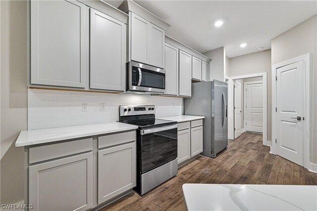 kitchen with stainless steel appliances, tasteful backsplash, gray cabinets, dark hardwood / wood-style flooring, and light stone counters