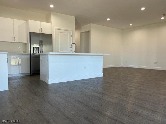 kitchen featuring an island with sink, sink, white cabinets, dark wood-type flooring, and black fridge