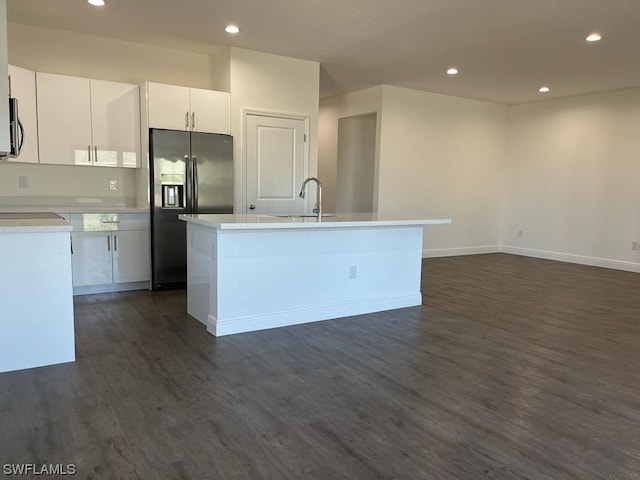 kitchen with white cabinets, stainless steel fridge, dark wood-type flooring, and a kitchen island with sink