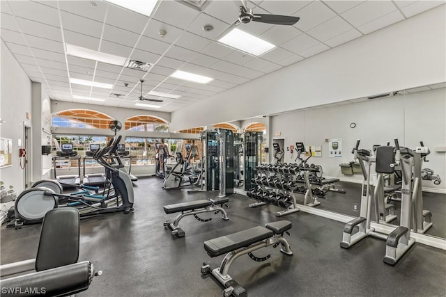 exercise room with a paneled ceiling, ceiling fan, and a towering ceiling