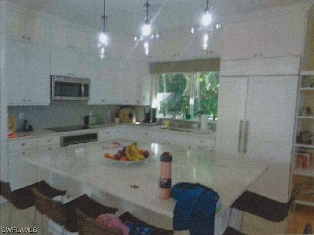 kitchen with white cabinets, cooktop, hanging light fixtures, and light stone counters