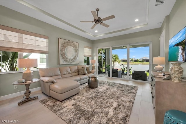 living room featuring a water view, a tray ceiling, a healthy amount of sunlight, and ceiling fan