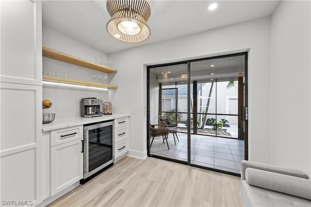 kitchen with beverage cooler, light stone countertops, light hardwood / wood-style floors, and white cabinetry