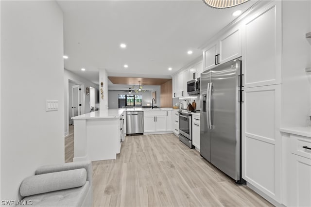 kitchen featuring kitchen peninsula, appliances with stainless steel finishes, beamed ceiling, white cabinetry, and light wood-type flooring