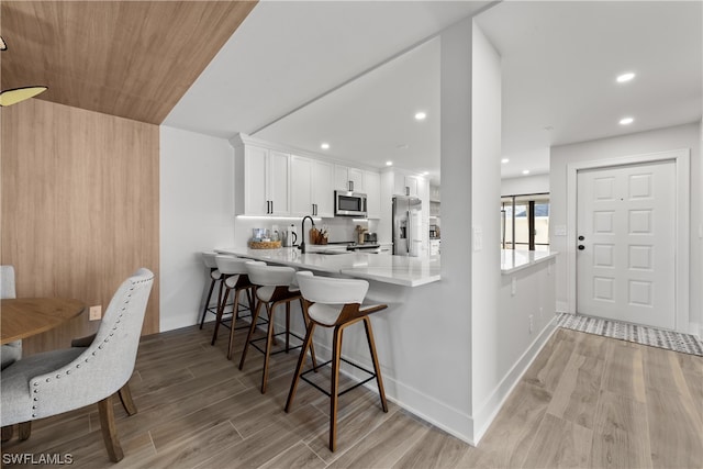 kitchen with kitchen peninsula, white cabinetry, a breakfast bar, appliances with stainless steel finishes, and light hardwood / wood-style floors