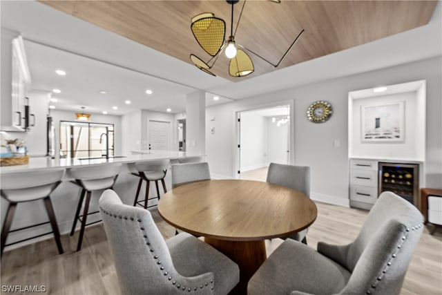 dining space with light hardwood / wood-style floors, wood ceiling, sink, and wine cooler