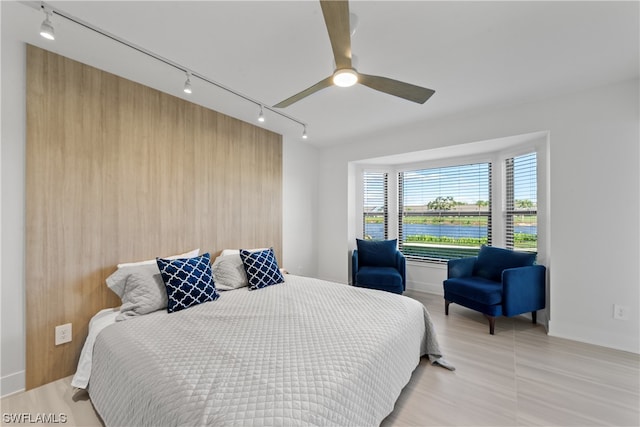 bedroom with rail lighting, wooden walls, and ceiling fan