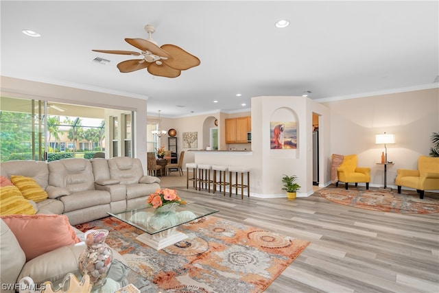 living room with ornamental molding, light wood-type flooring, and ceiling fan with notable chandelier