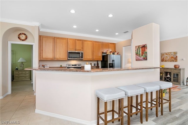 kitchen featuring stainless steel appliances, crown molding, a breakfast bar area, light stone countertops, and light tile floors