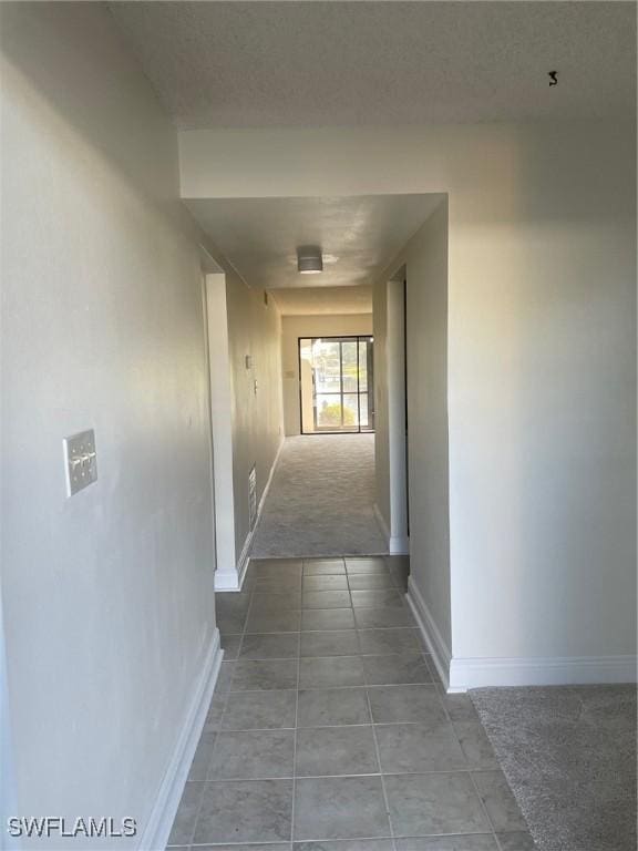 hall featuring light colored carpet, light tile patterned flooring, a textured ceiling, and baseboards