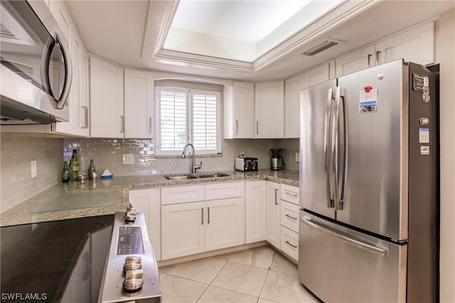 kitchen with sink, white cabinets, stainless steel appliances, a tray ceiling, and light stone countertops