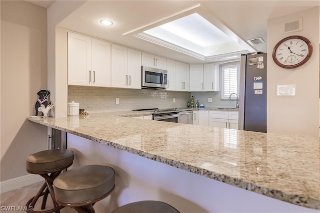 kitchen featuring white cabinets, appliances with stainless steel finishes, light stone counters, and a breakfast bar