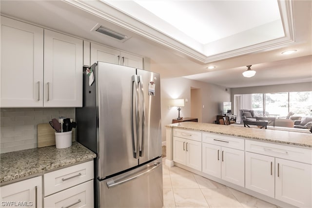 kitchen with white cabinets, light stone countertops, backsplash, and stainless steel fridge