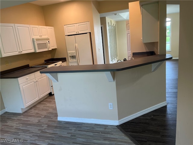 kitchen with kitchen peninsula, white cabinetry, white appliances, and hardwood / wood-style flooring