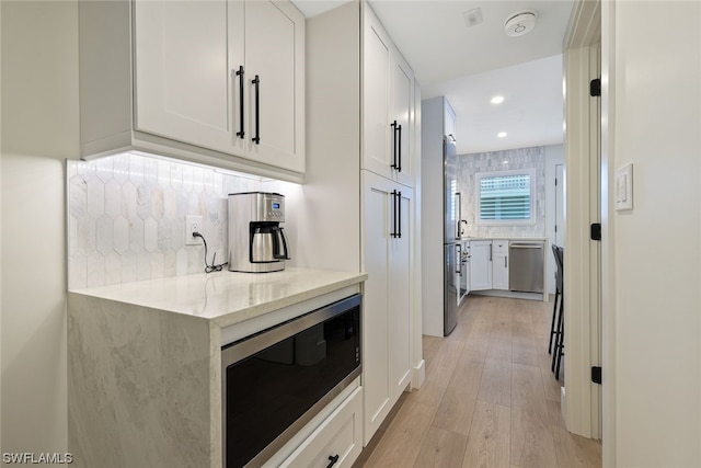 kitchen with appliances with stainless steel finishes, light stone counters, light hardwood / wood-style floors, white cabinets, and backsplash