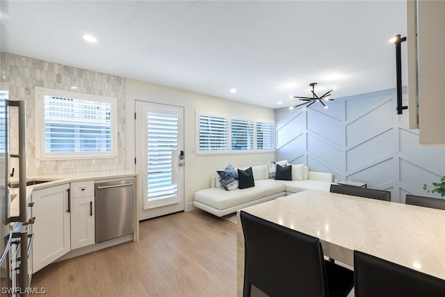 kitchen featuring a notable chandelier, stainless steel dishwasher, white cabinetry, and light wood-type flooring