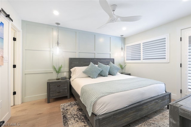 bedroom with a barn door, ceiling fan, and light wood-type flooring