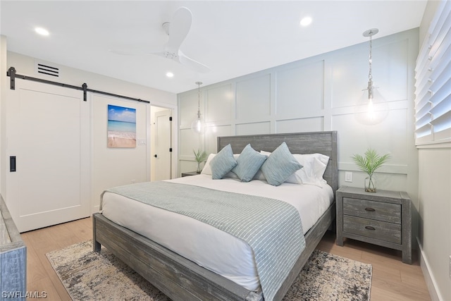 bedroom featuring a barn door, ceiling fan, and light wood-type flooring