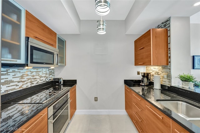 kitchen with pendant lighting, dark stone countertops, appliances with stainless steel finishes, tasteful backsplash, and light tile patterned flooring