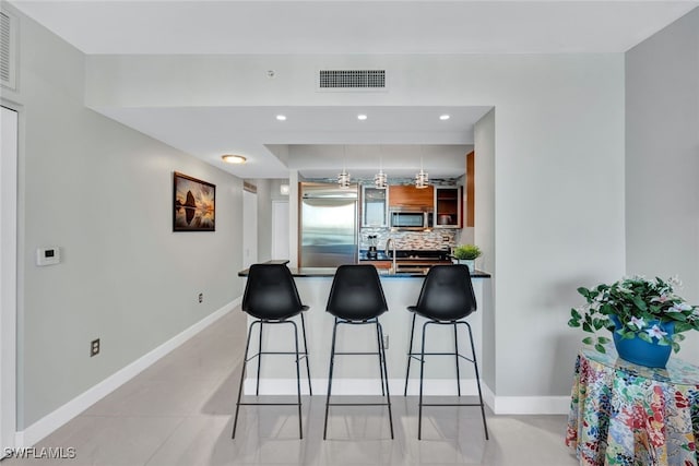 kitchen featuring stainless steel appliances, backsplash, kitchen peninsula, a breakfast bar, and light tile patterned flooring