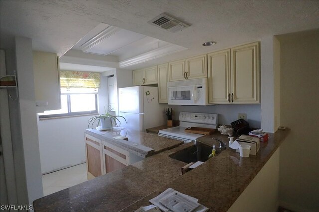 kitchen with visible vents, dark stone counters, cream cabinets, white appliances, and a raised ceiling