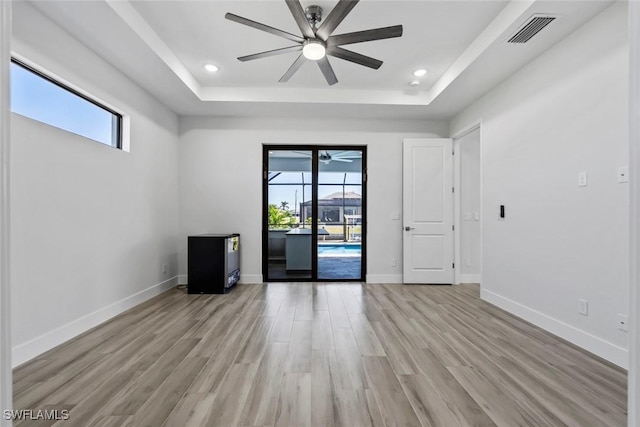 spare room with ceiling fan, light wood-type flooring, and a tray ceiling