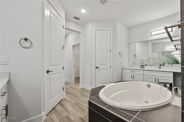 bathroom featuring vanity, tiled tub, and wood-type flooring