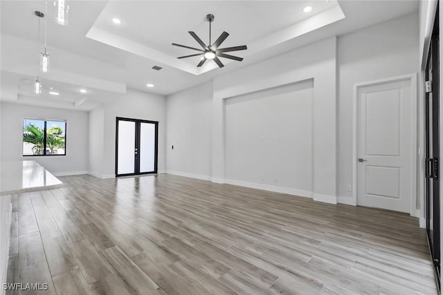 unfurnished living room featuring a tray ceiling, french doors, ceiling fan, and light wood-type flooring