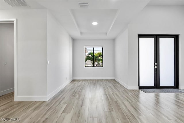 spare room with a tray ceiling, light hardwood / wood-style flooring, and french doors