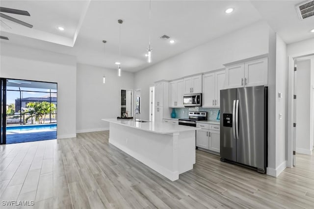 kitchen with stainless steel appliances, an island with sink, pendant lighting, and white cabinets