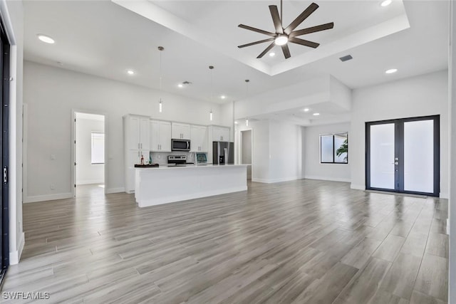 unfurnished living room with ceiling fan, a high ceiling, a tray ceiling, light hardwood / wood-style floors, and french doors