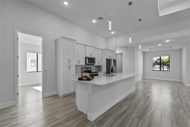 kitchen featuring white cabinetry, a large island with sink, hanging light fixtures, light hardwood / wood-style floors, and stainless steel appliances