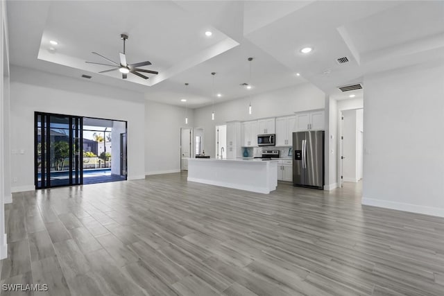 unfurnished living room featuring a tray ceiling, light hardwood / wood-style flooring, ceiling fan, and a towering ceiling