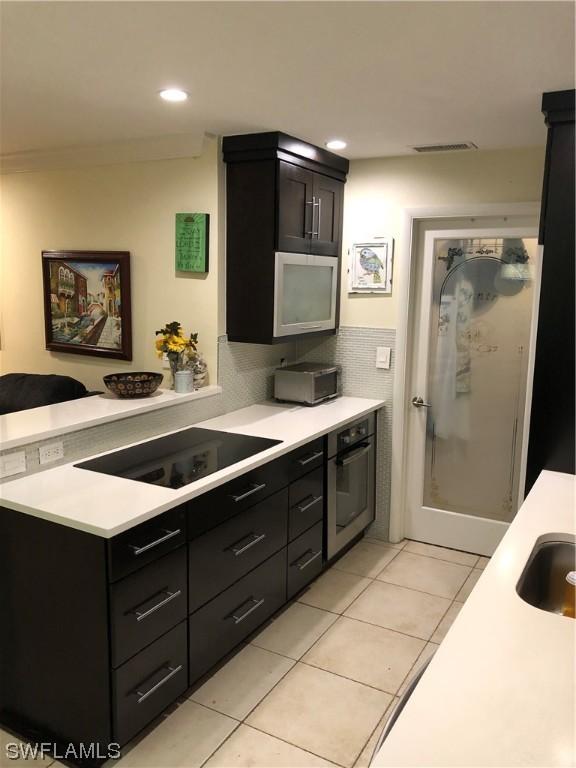 kitchen featuring kitchen peninsula, oven, black electric stovetop, light tile patterned flooring, and tile walls