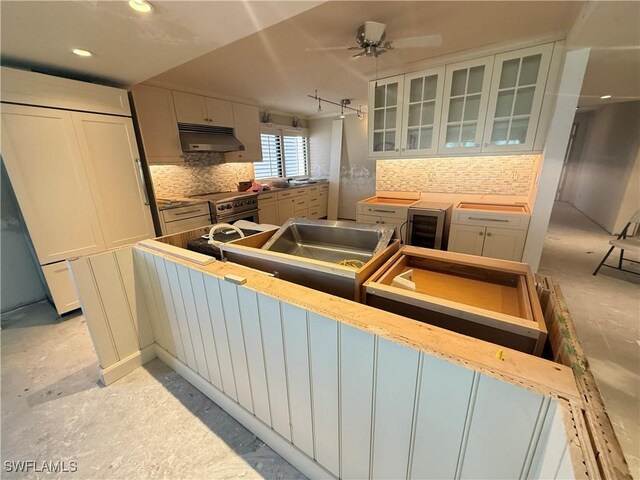 kitchen with high end range, ceiling fan, tasteful backsplash, and white cabinets